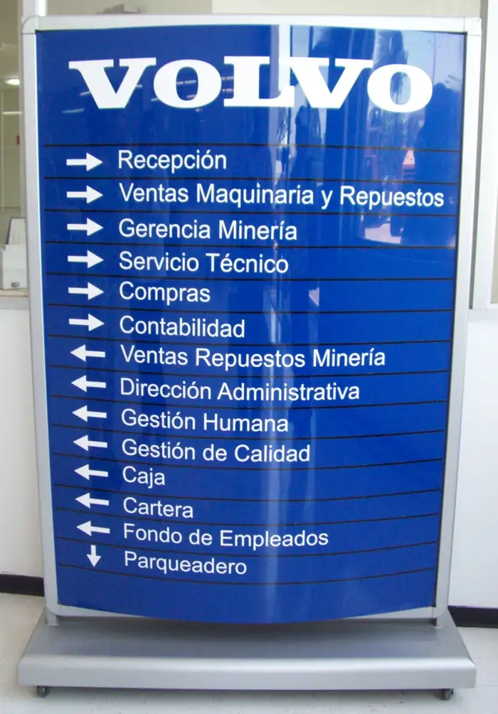 Tótem direccional azul con la marca Volvo y el listado de áreas de la sede: recepción, ventas de maquinaria y repuestos, servicio técnico, contabilidad, gestión humana y parqueadero