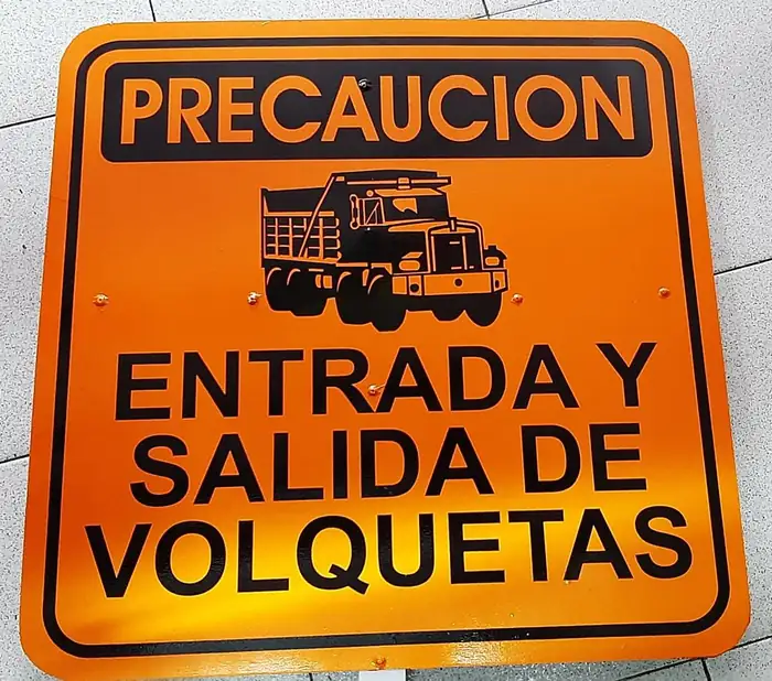 Señal de precaución fabricada en lámina naranja, con pictograma de volqueta y el texto «Entrada y salida de volquetas»